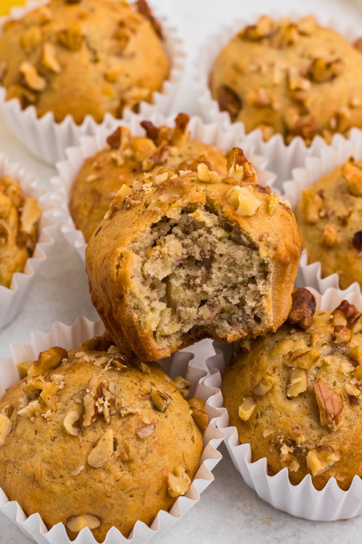 Light golden brown banana bread muffins in white liners, topped with chopped pecans.