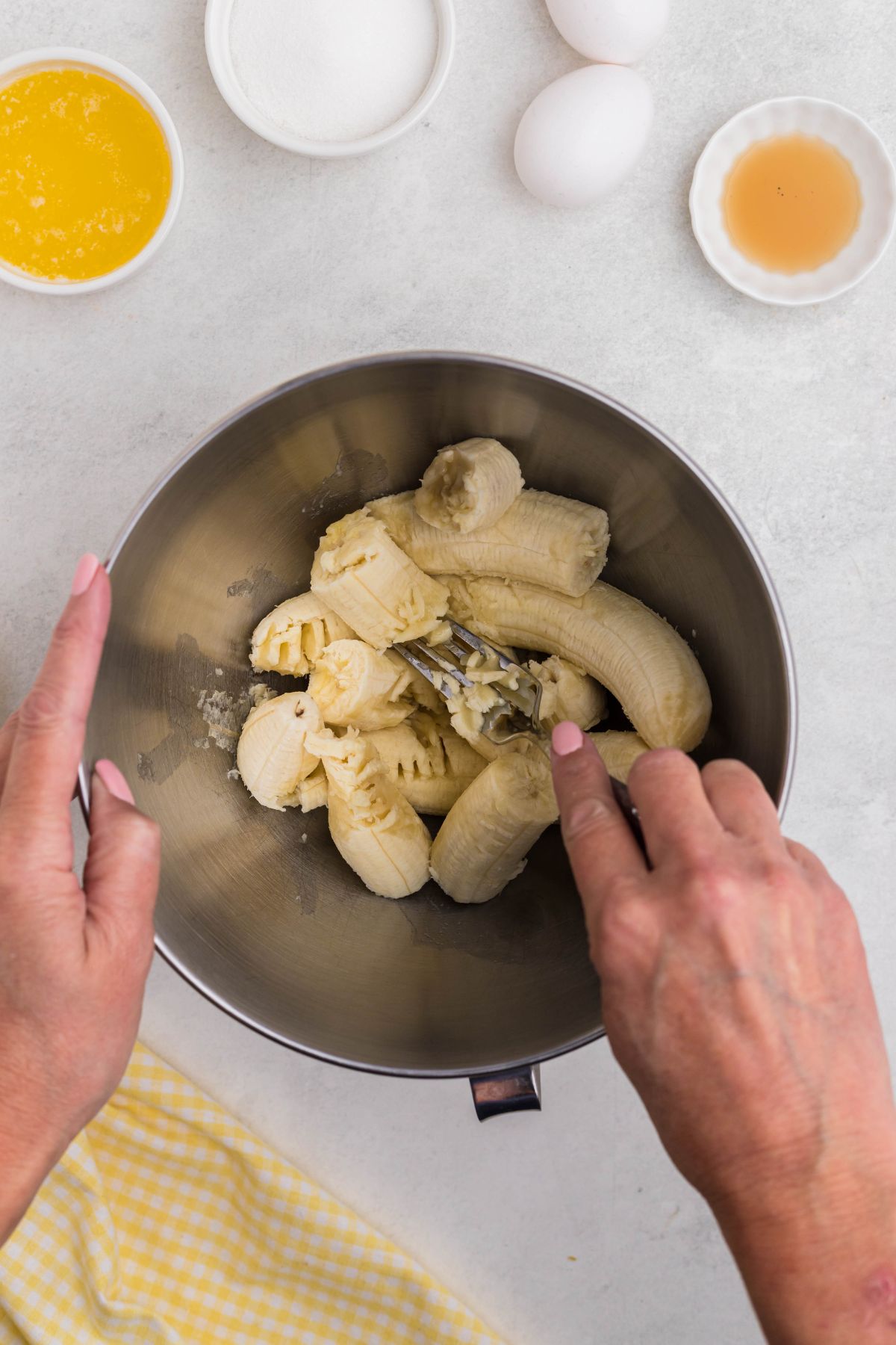 Large silver bowl with bananas being mashed with fork.