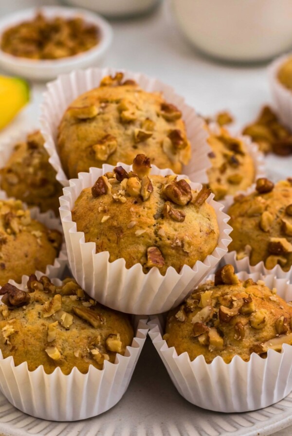 Light golden brown banana bread muffins in white liners, topped with chopped pecans.