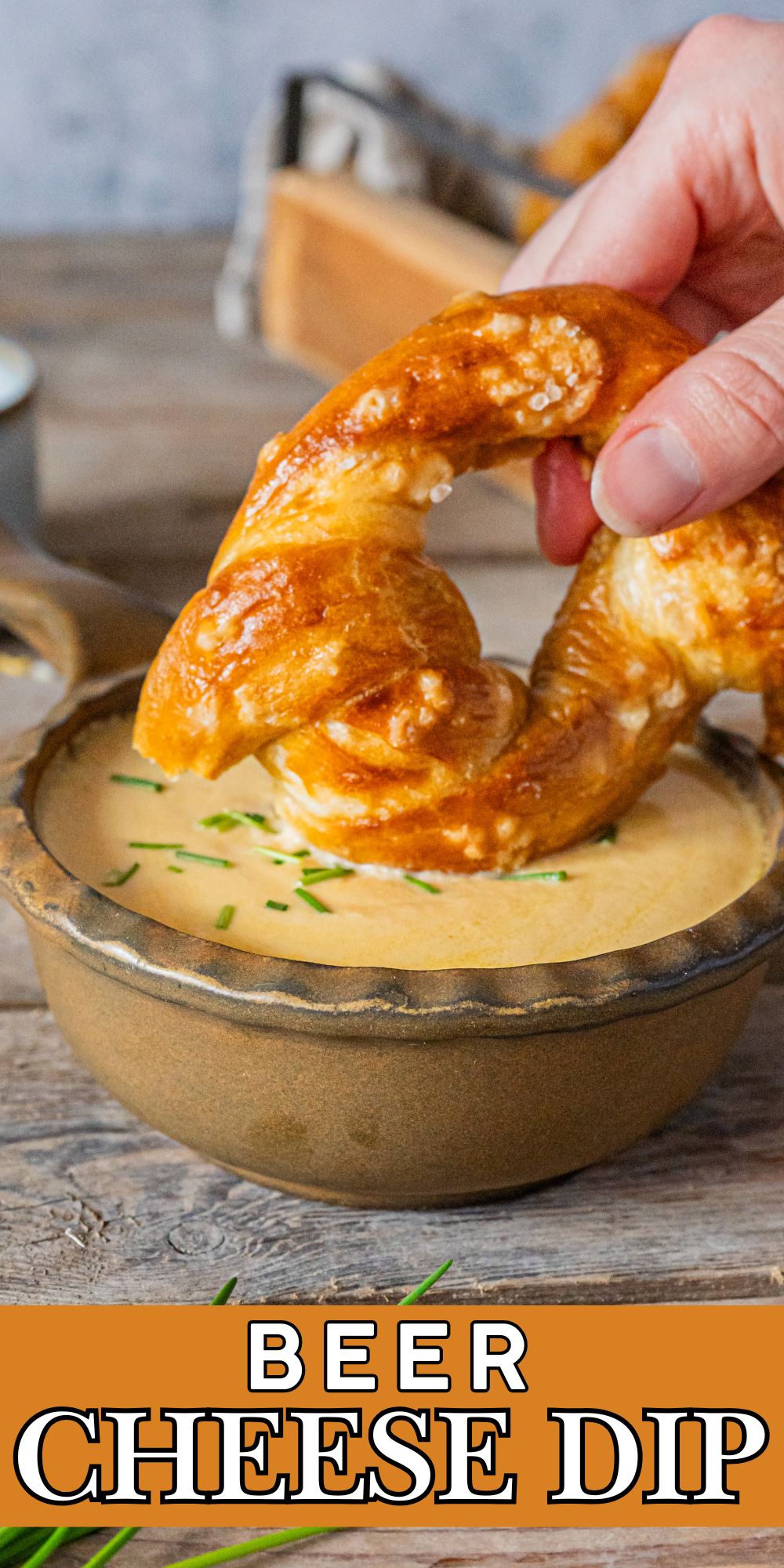 A small bowl of cheese with a soft pretzel being dipped into the cheese.