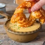 A small brown bowl with melted cheese dip, with a soft pretzel being dipped into the cheese.