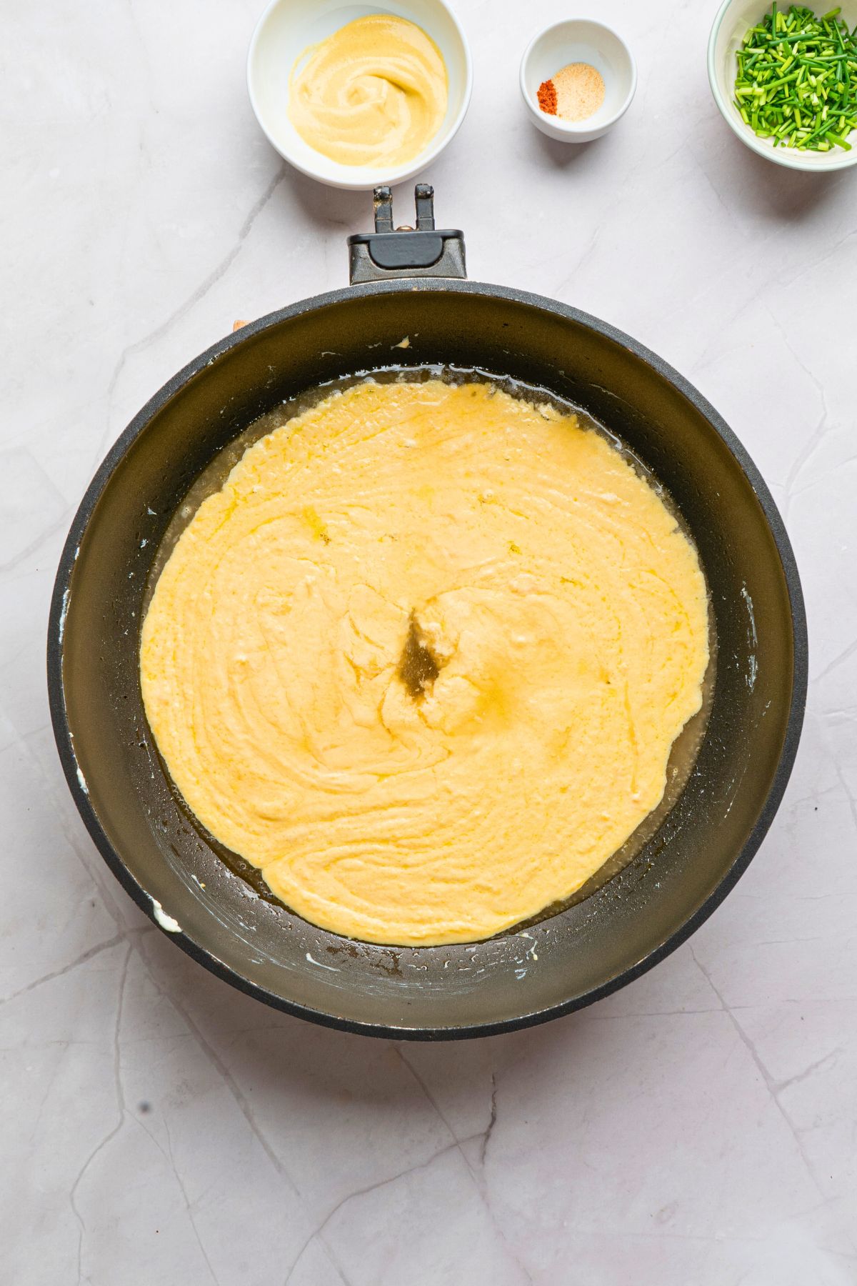 Cheeses being melted in a saucepan with other seasonings on the table. 