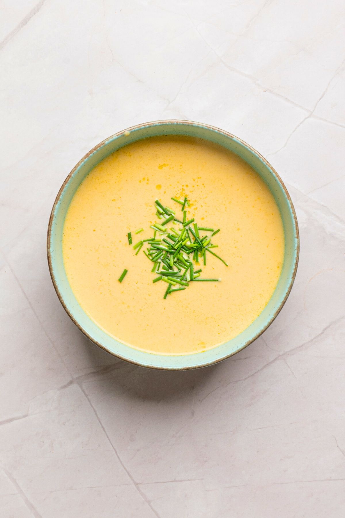 Small bowl of melted beer cheese dip topped with chopped chives. 