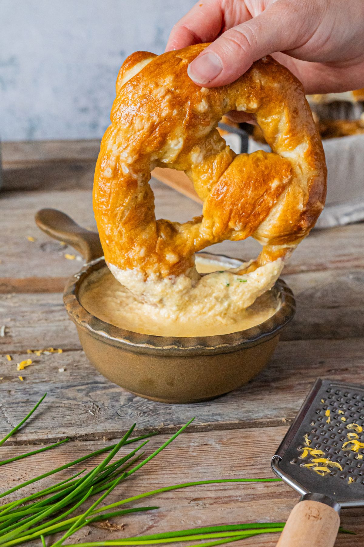 A small bowl of cheese with a soft pretzel being dipped into the cheese.