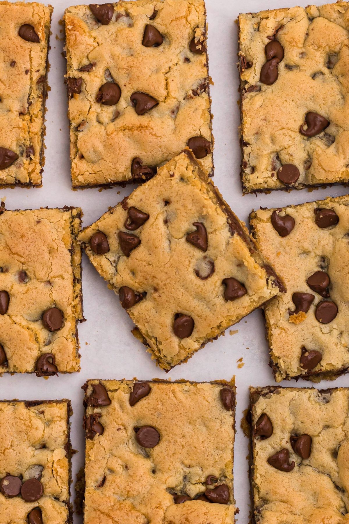 Chocolate chip cookie bars cut into slices, on a white marble table. 
