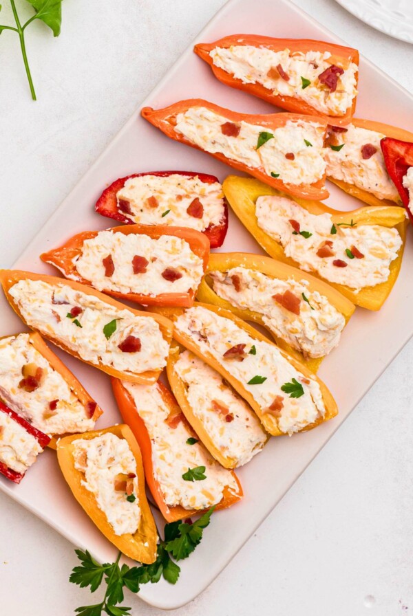 Stuffed cream cheese peppers on a rectangle white plate.