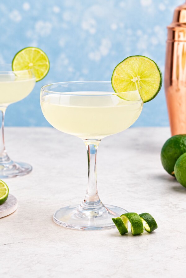 Coupe glass filled with drink, garnished with lime wheel, on a marble table with a blue backdrop.