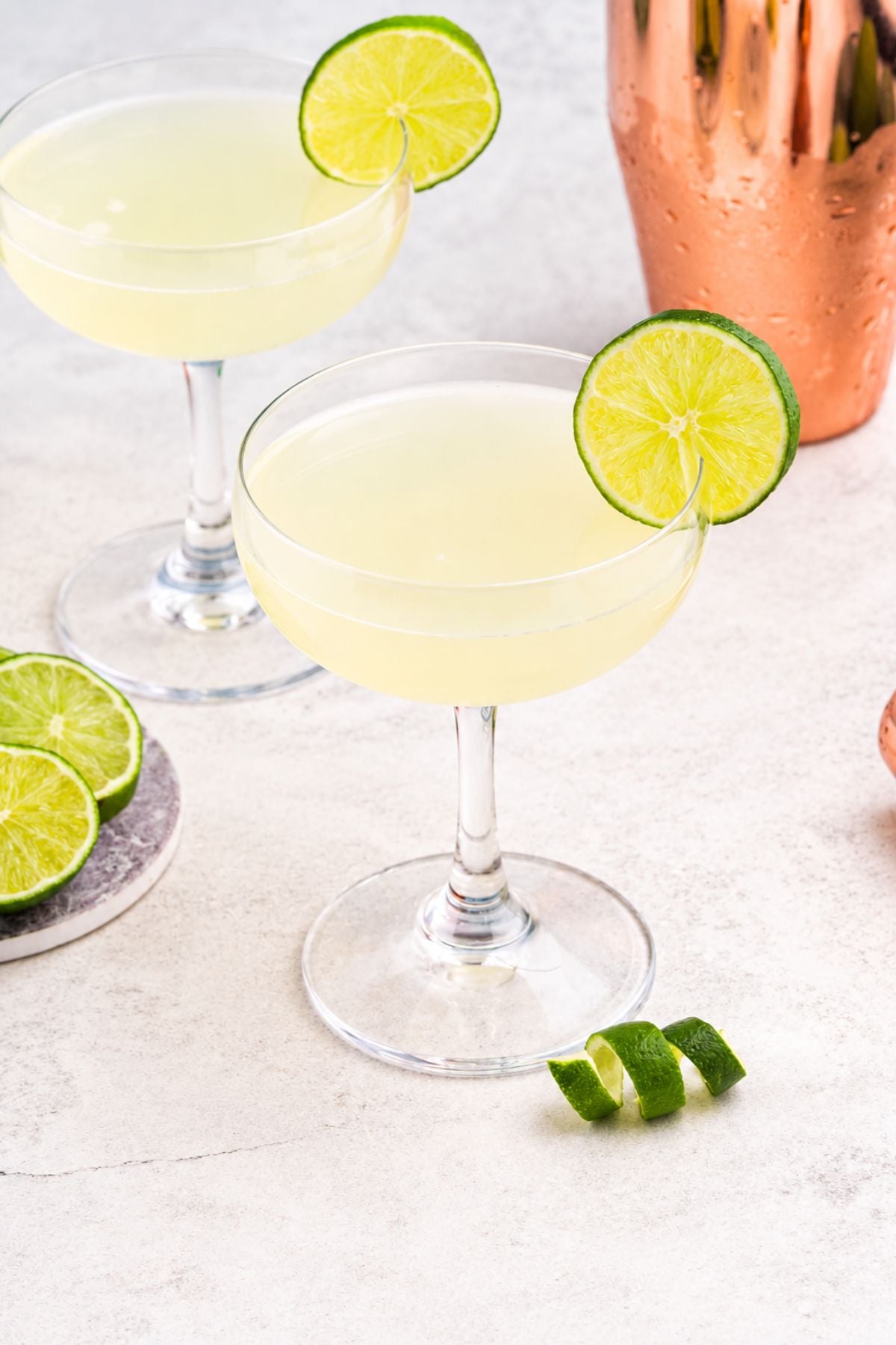 Coupe glass filled with drink, garnished with lime wheel, on a marble table with a blue backdrop.