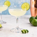 Coupe glass filled with drink, garnished with lime wheel, on a marble table with a blue backdrop.