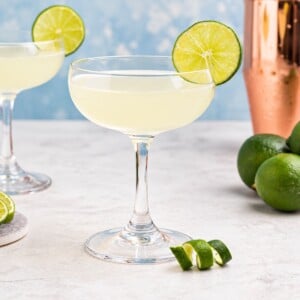 Coupe glass filled with drink, garnished with lime wheel, on a marble table with a blue backdrop.