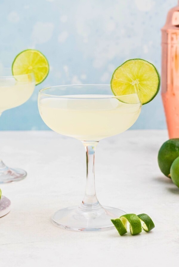 Coupe glass filled with drink, garnished with lime wheel, on a marble table with a blue backdrop.