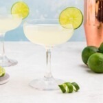Coupe glass filled with drink, garnished with lime wheel, on a marble table with a blue backdrop.