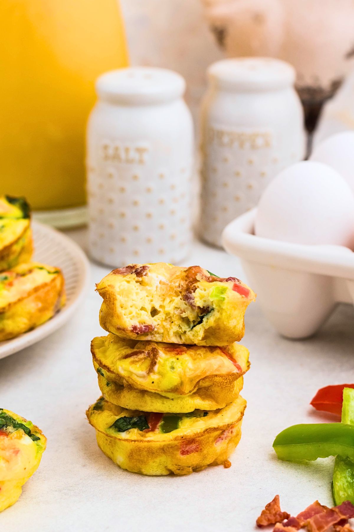 Three egg bites stacked together with one having a bite out of it, on a marble table in front of other eggs and juice.
