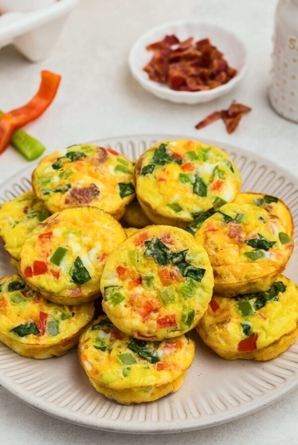 Bright yellow egg bites with red and green chopped bell peppers baked inside, on a round cream plate.