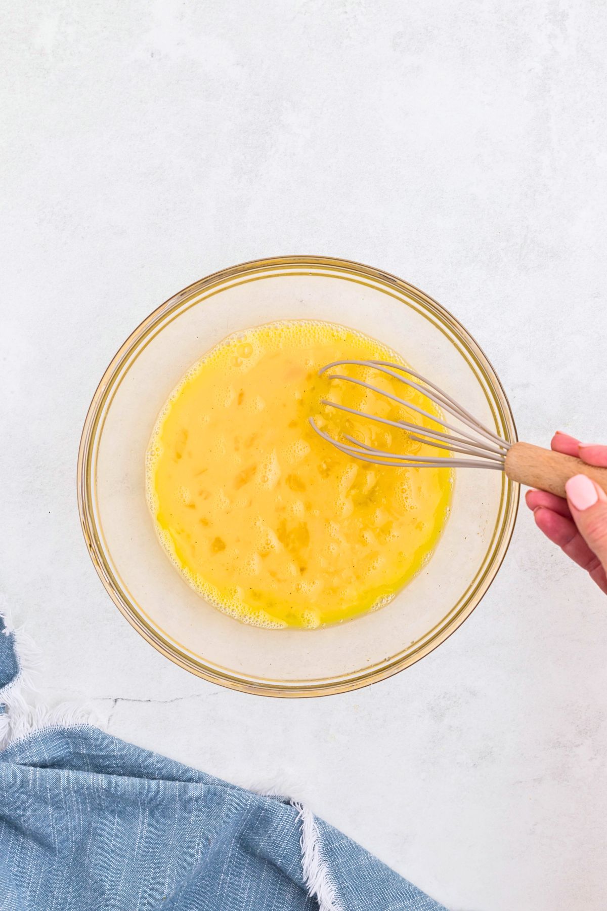 Eggs and seasonings being whisked together with milk  in a clear glass bowl. 