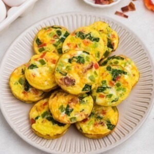 Bright yellow egg bites with red and green chopped bell peppers baked inside, on a round cream plate.