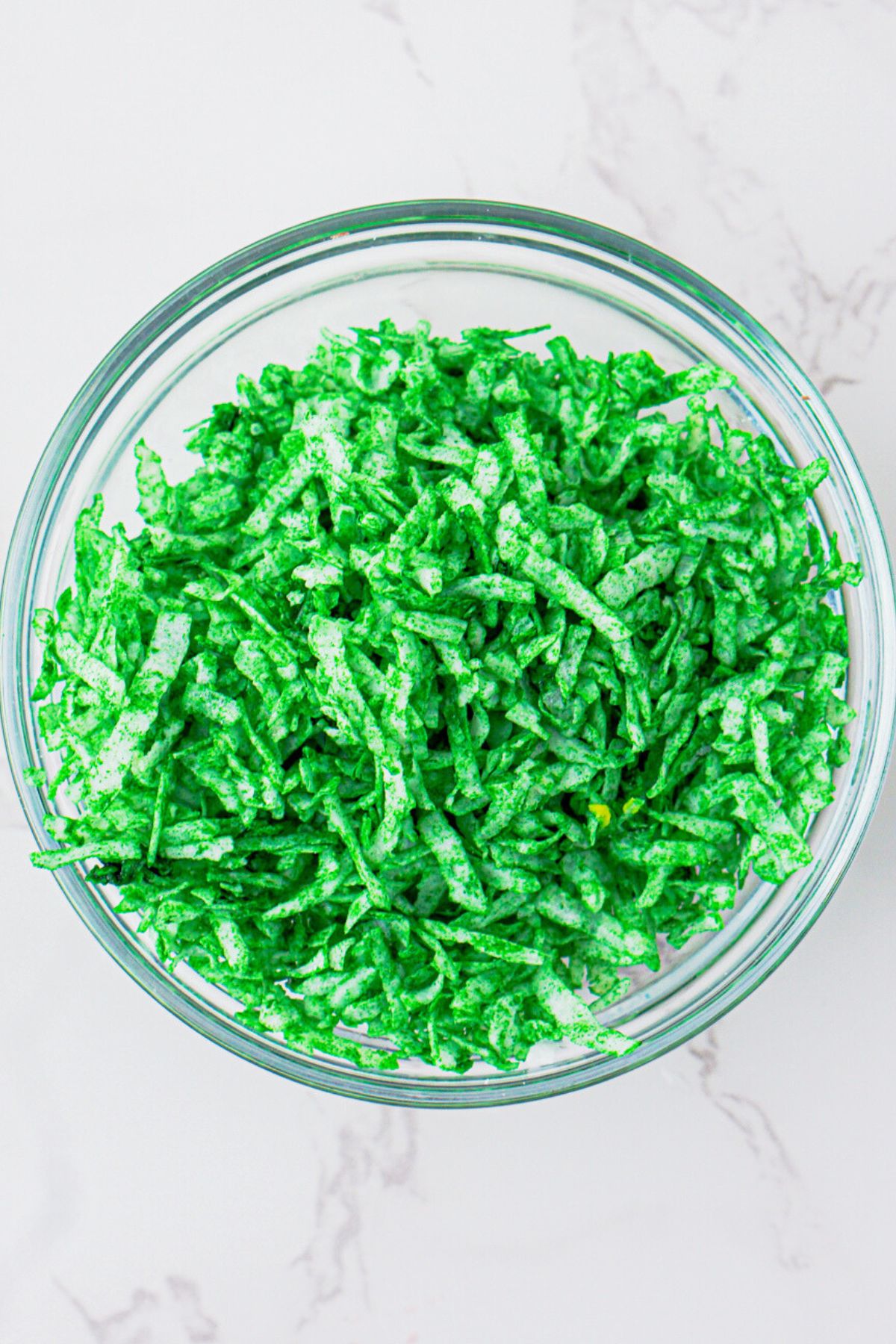 Shredded coconut with green food coloring added, in a clear glass bowl. 