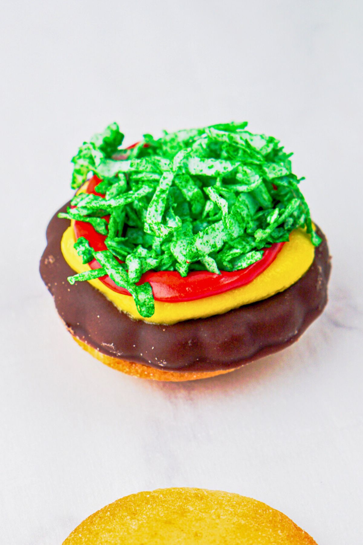 Wafer and chocolate cookies, topped with red and yellow icing, and green shredded coconut, on a white marble board. 