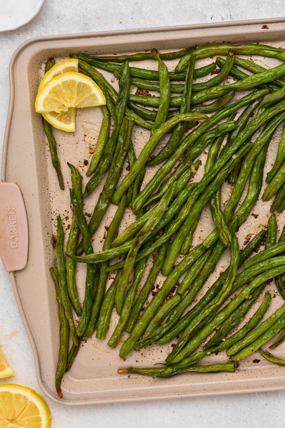 Roasted green beans seasoned on a baking sheet and then drizzled with fresh lemon juice. 