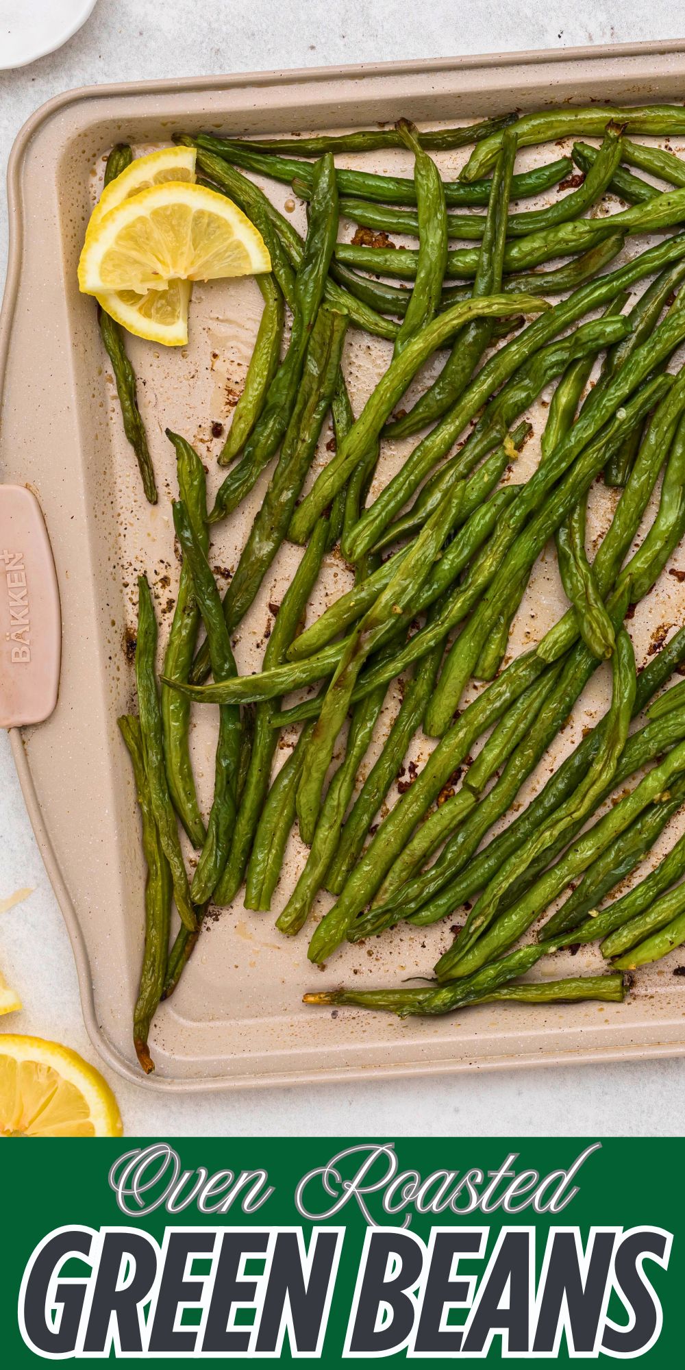 Roasted green beans seasoned on a baking sheet and then drizzled with fresh lemon juice.