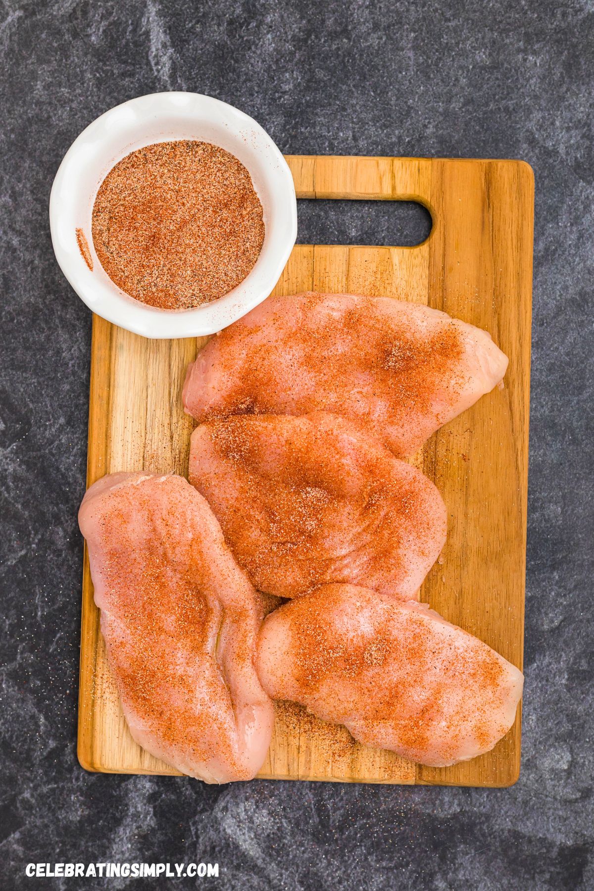 Seasoned chicken breast on a wooden cutting board, before being cooked. 