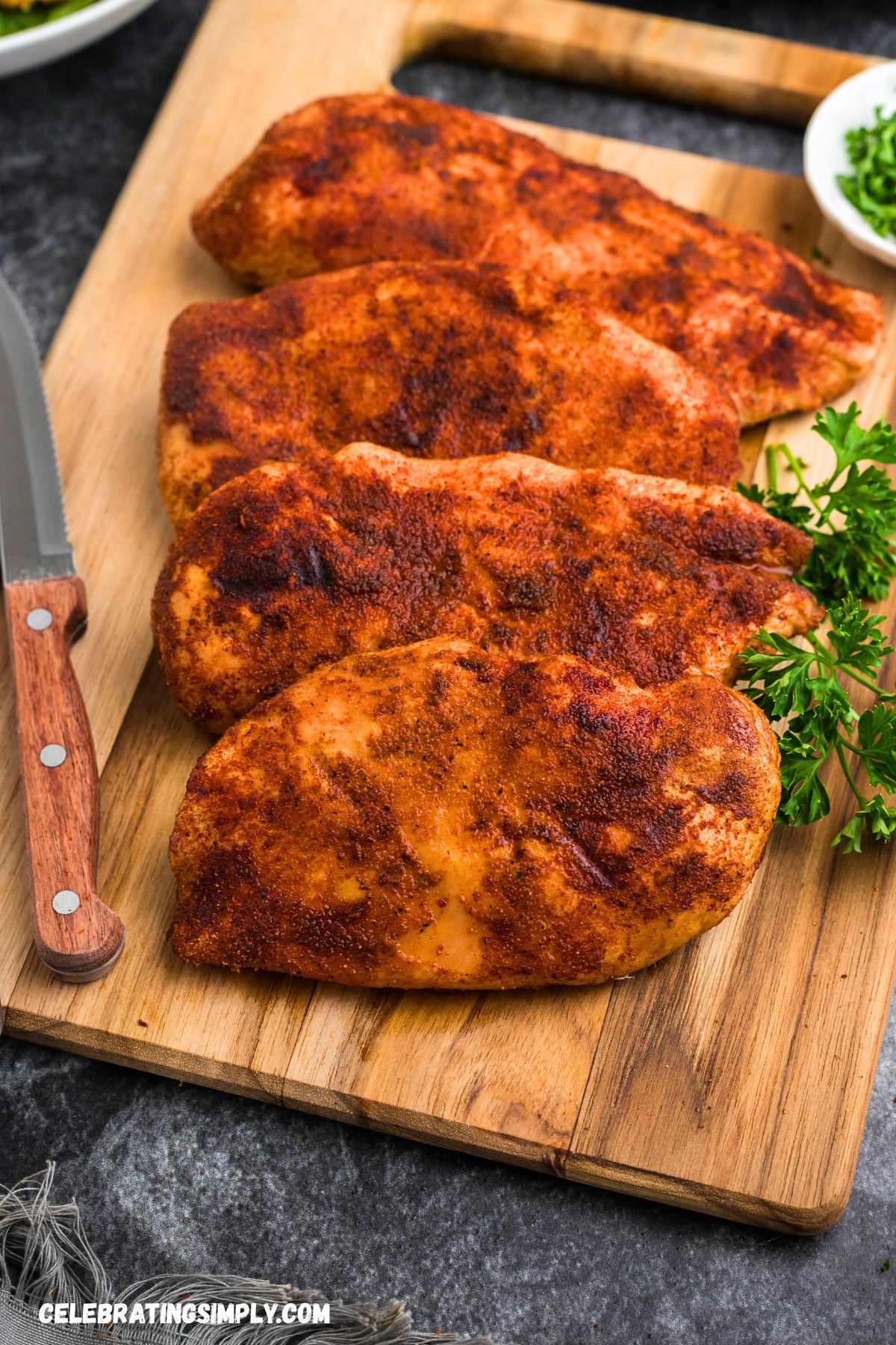 Seasoned, smoked chicken breasts on a wooden cutting board, resting in their juices. 