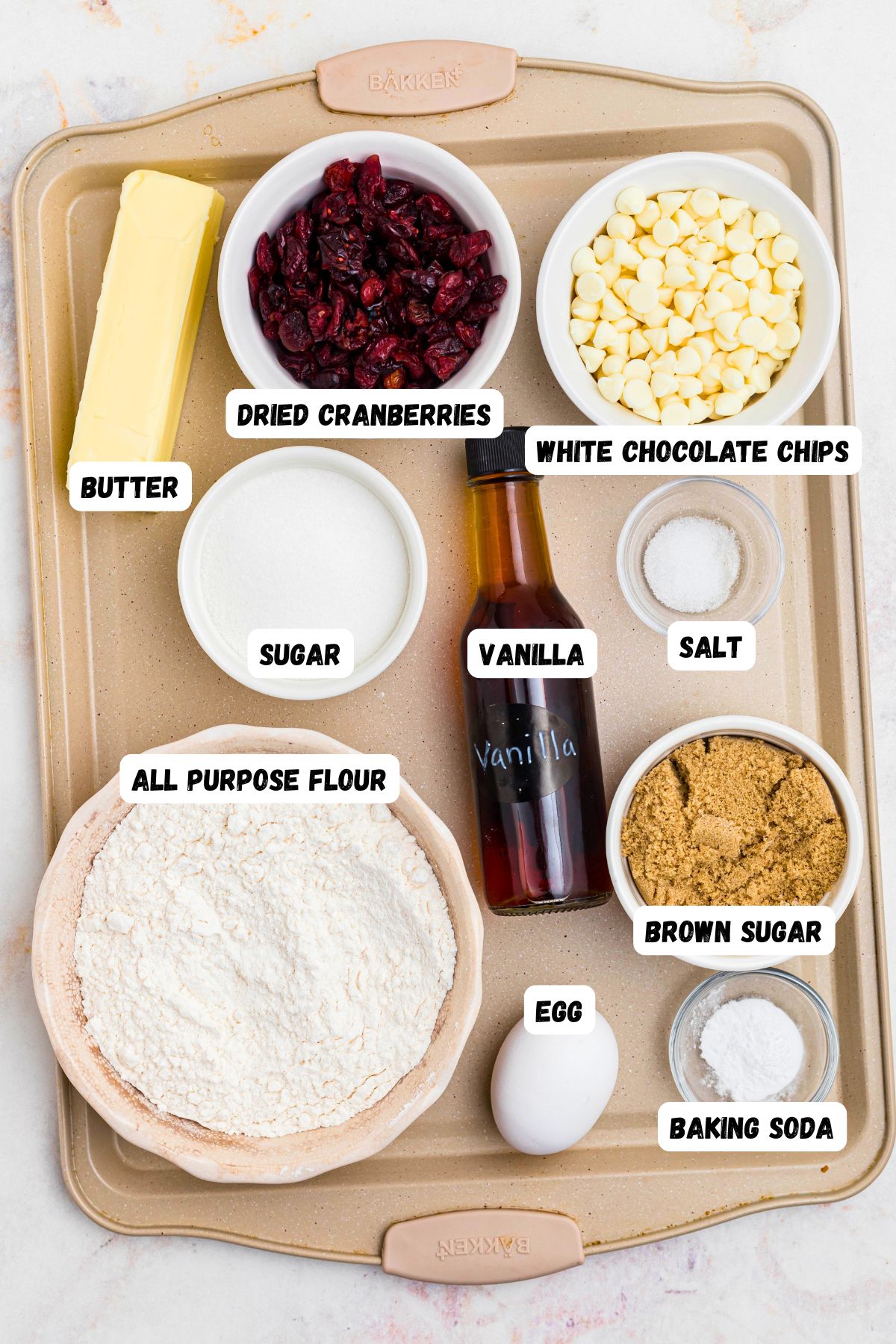 Ingredients needed to make cookies measured into small bowls on a baking sheet on a marble table. 