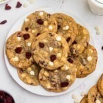 White chocolate chip and cranberry cookies stacked on a white plate with glasses of milk on the table.