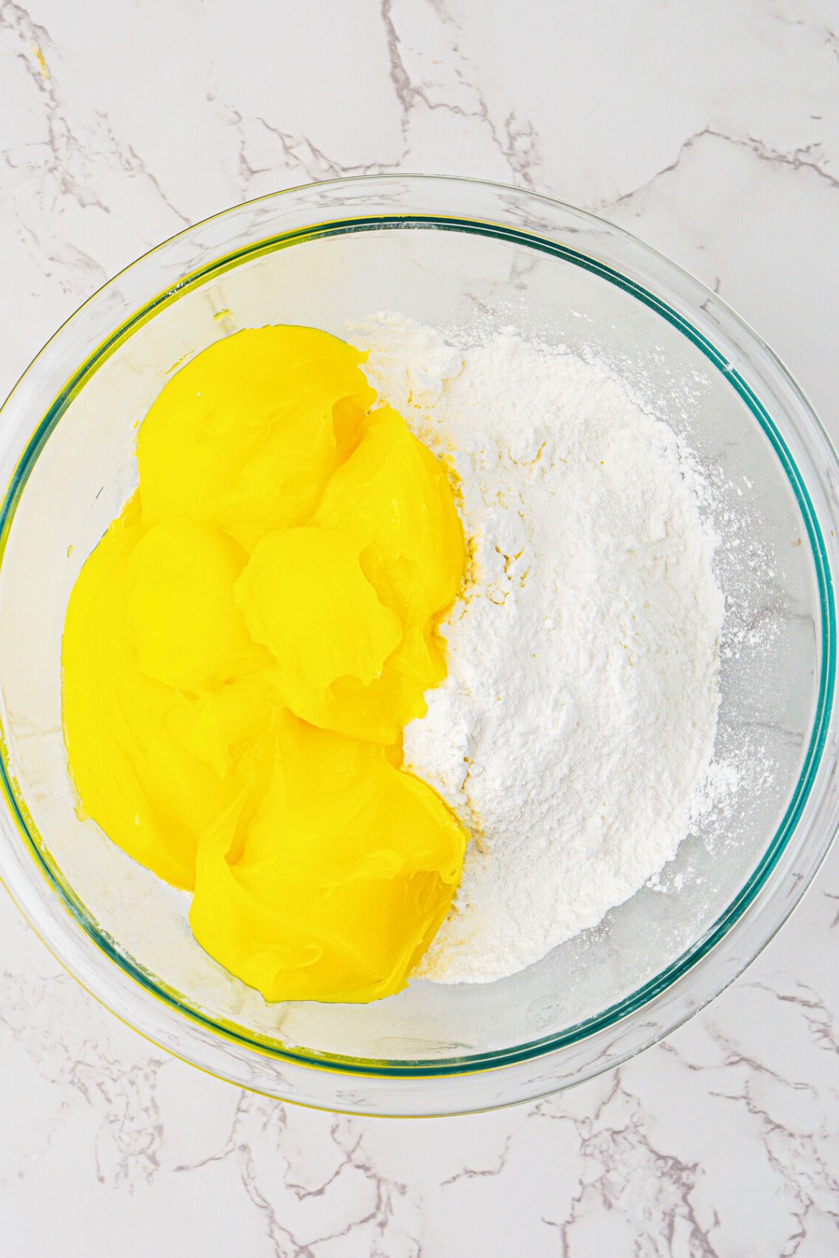 Cake mix and lemon pie filling being mixed together in a clear glass bowl. 