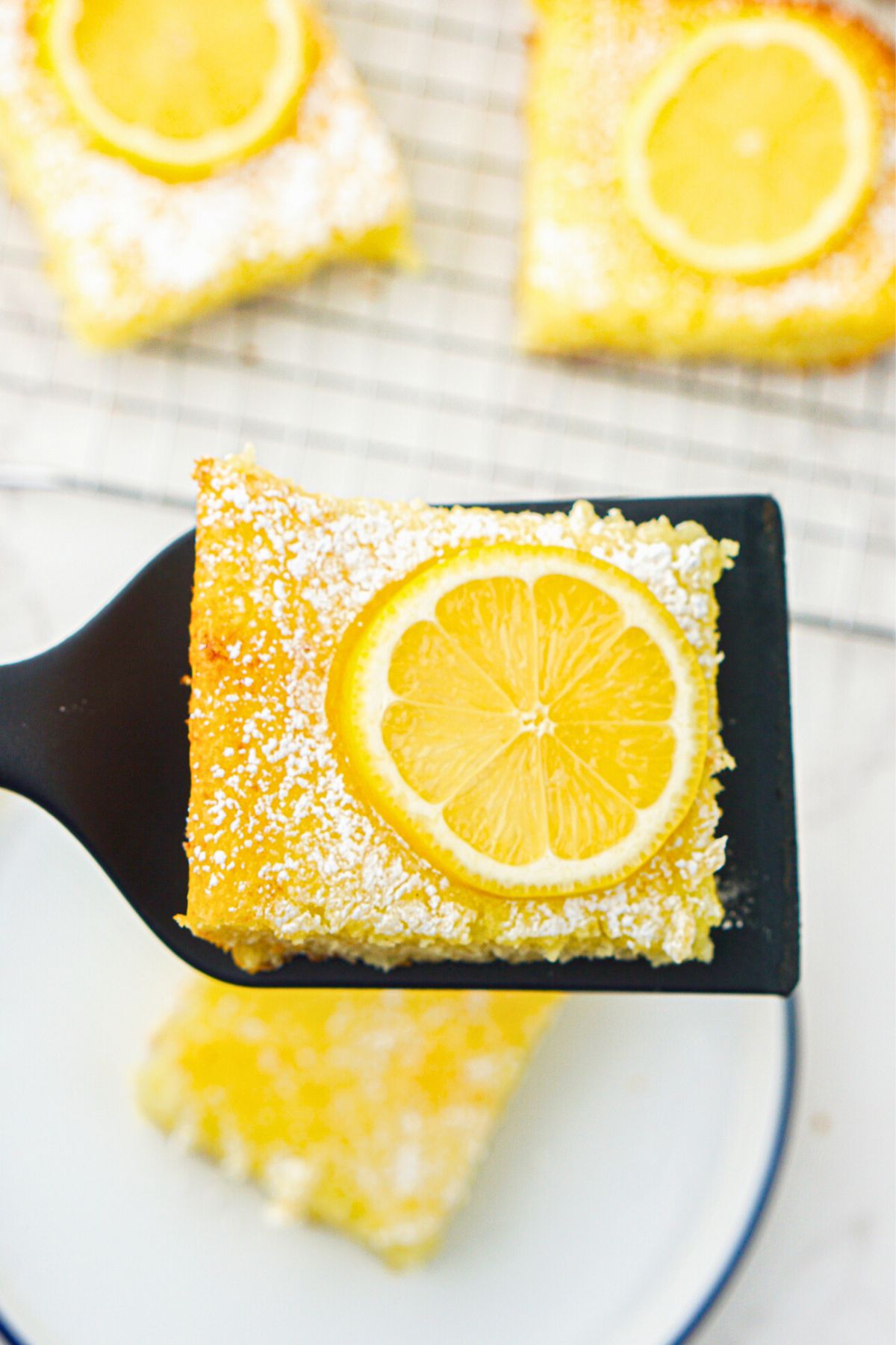 Bright yellow lemon bars  after baking, with one being lifted to serve on a spatula. 