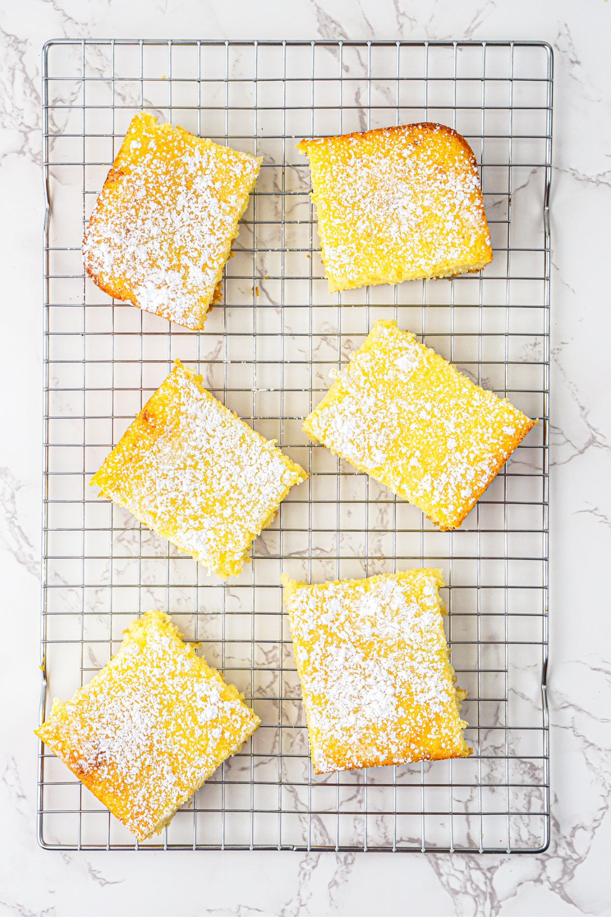 Bright yellow lemon bars baked and cooling on a wire rack. 