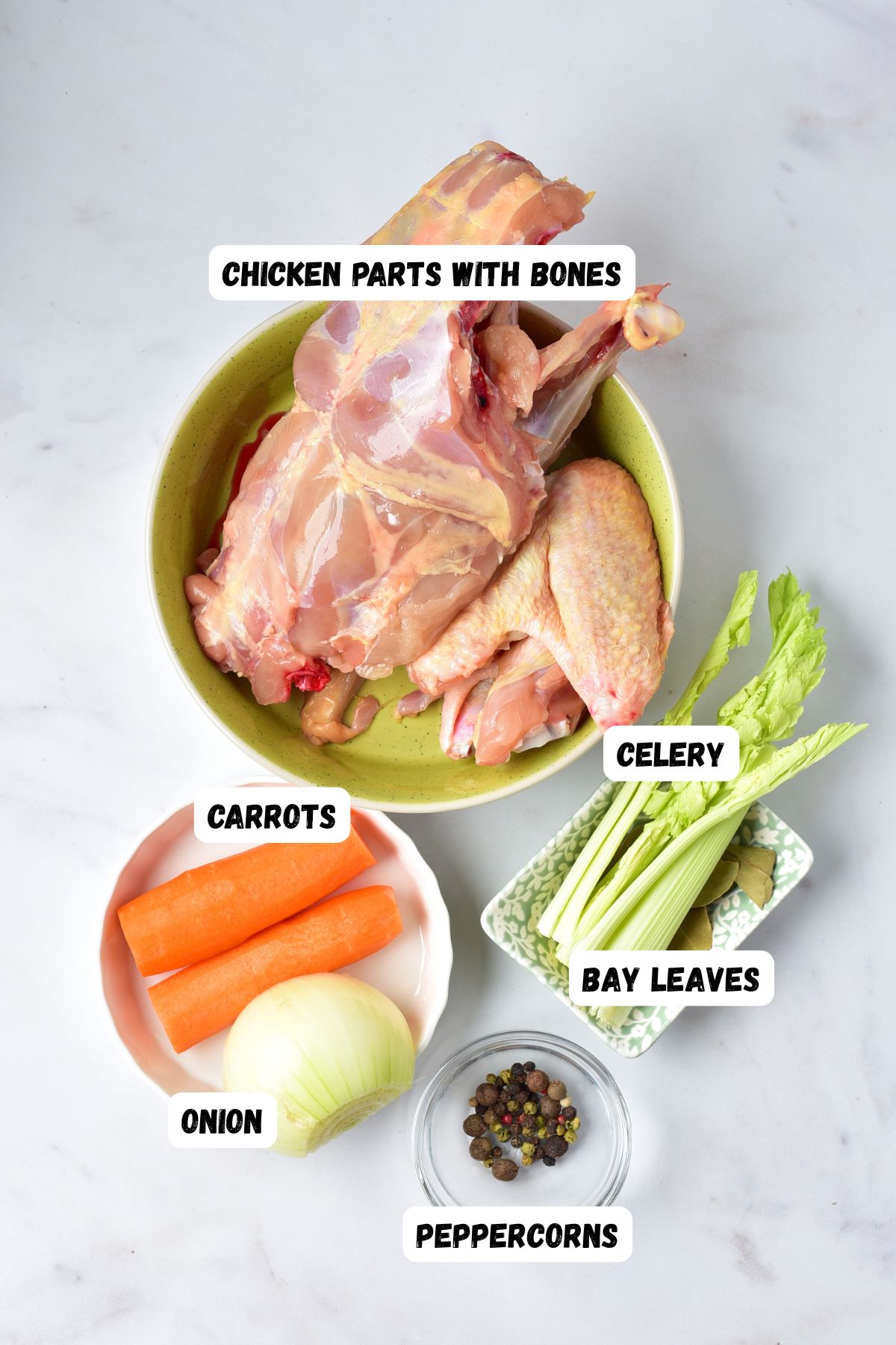 Ingredients needed to make chicken stock measured into small bowls on a white marble table. 