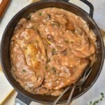 Creamy sauce over 3 pieces of cooked chicken in a large black skillet.