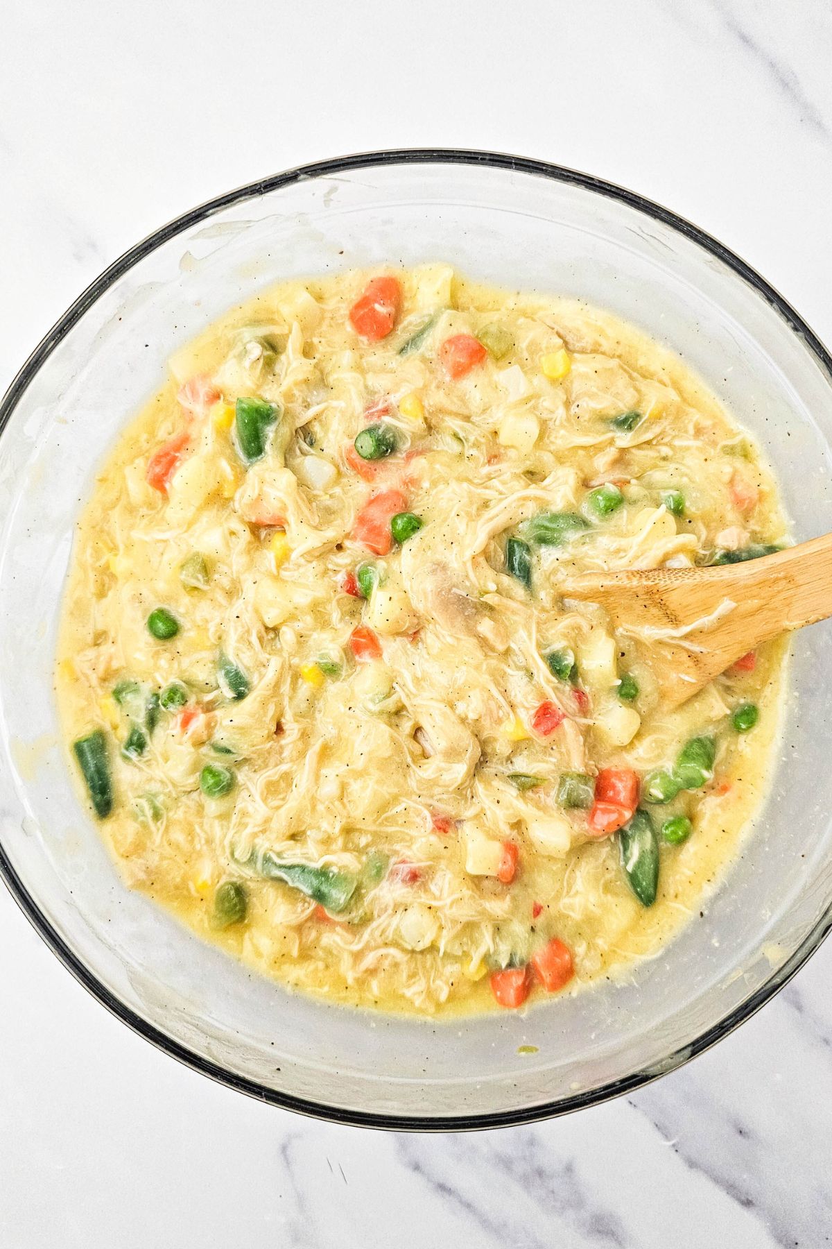 Creamy pot pie filling of soup, veggies, and shredded chicken, mixed in a clear glass bowl. 