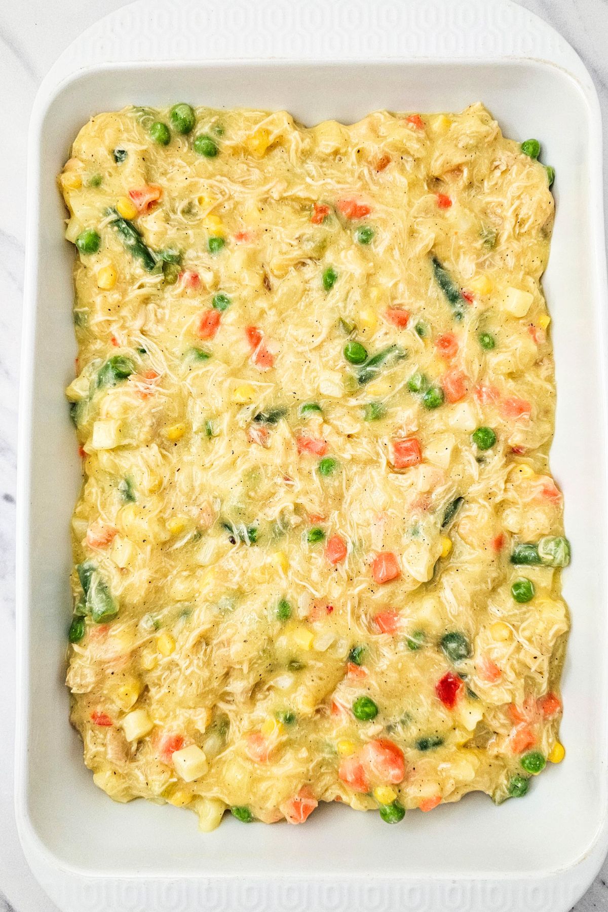 Pot pie filling topping a baked crust, in a rectangle white casserole dish. 