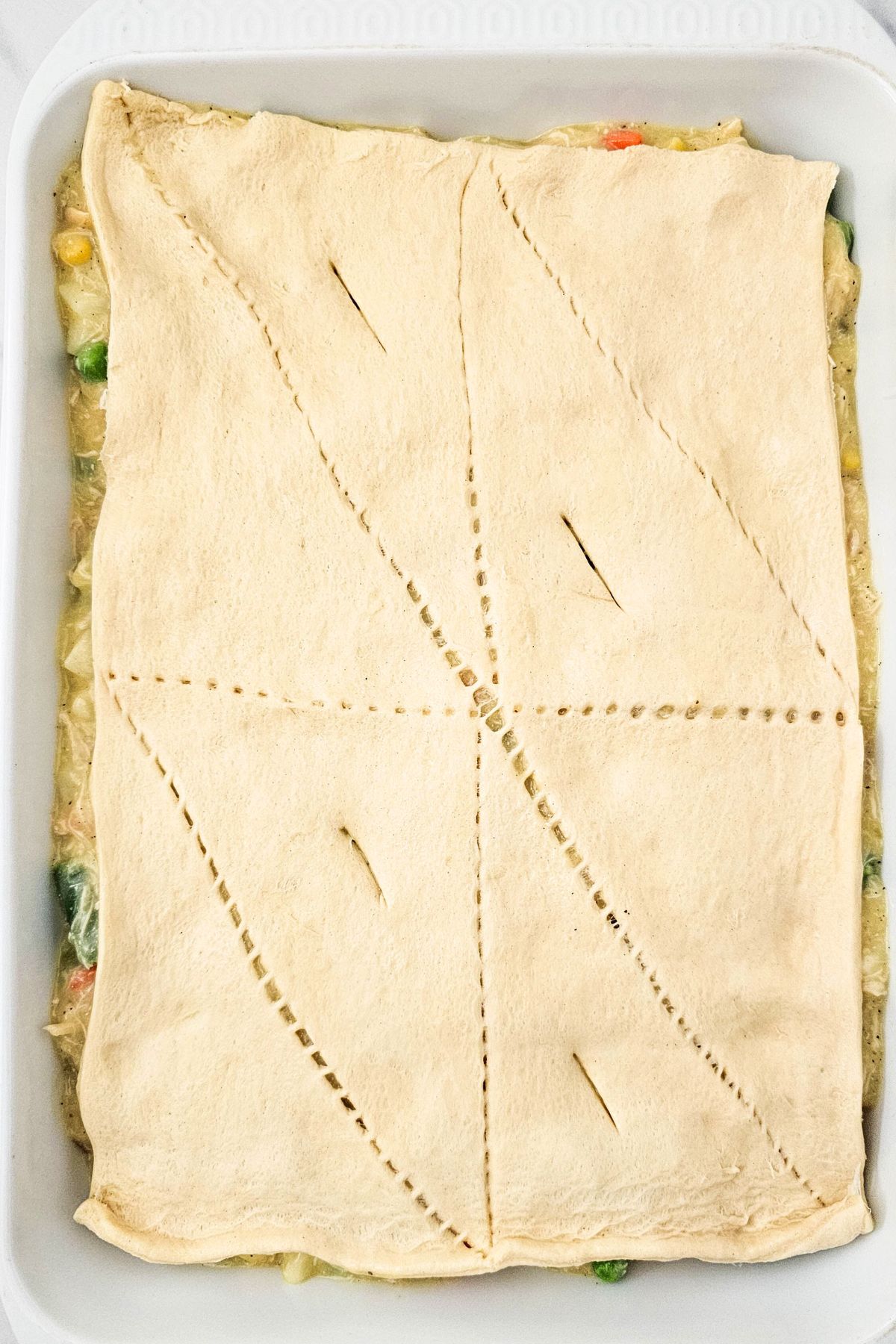 Casserole topped with rolled out unbaked crescent roll dough. 