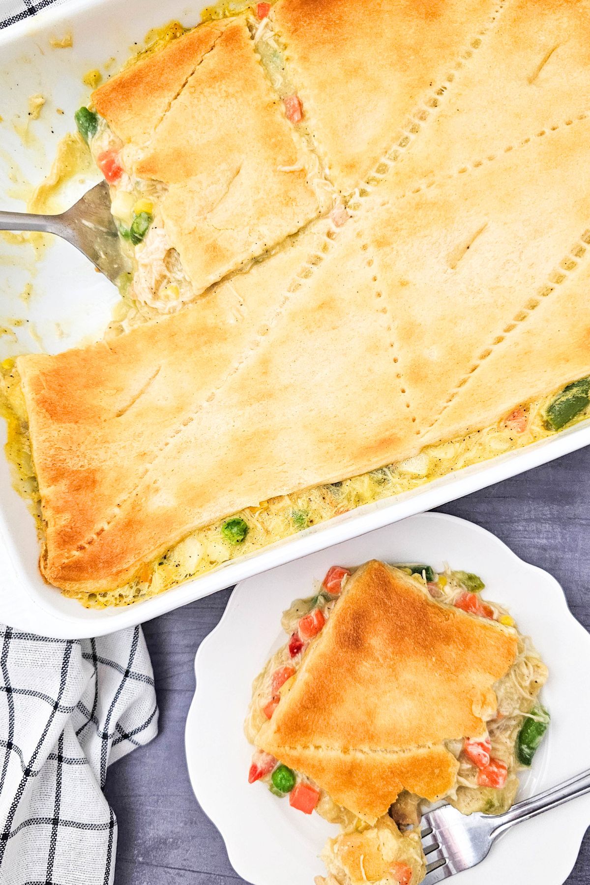 Golden crusted chicken pot pie in a casserole dish with a small slice on a white plate. 