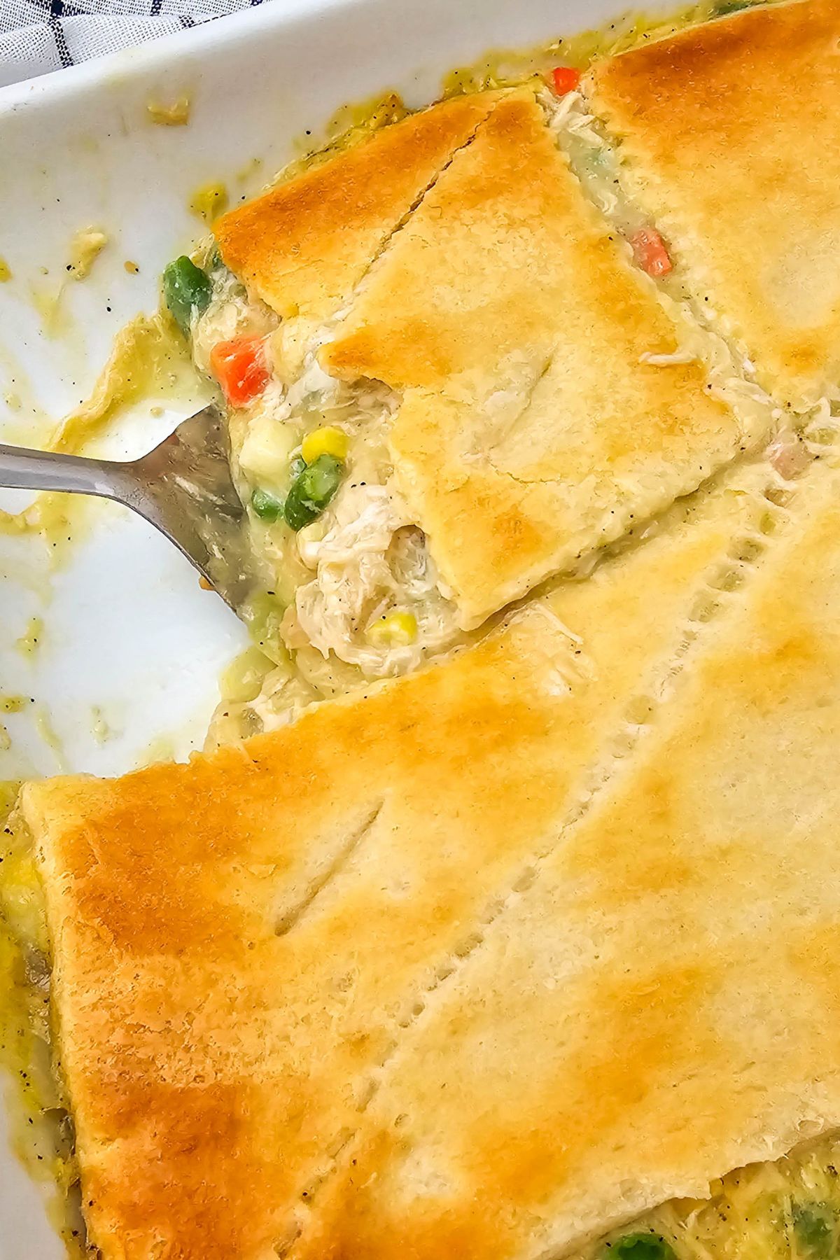 Golden crusted pot pie in a casserole dish with one slice being removed by a spatula. 