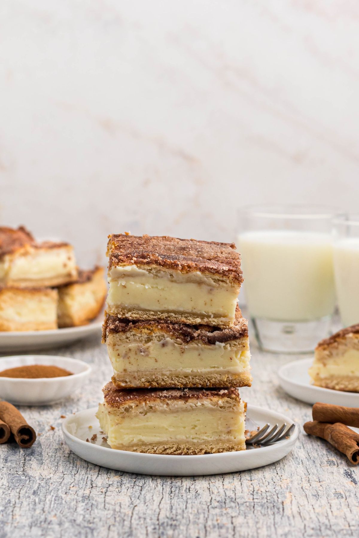 Three slices of cheesecake, stacked on a small white plate in front of glasses of milk. 
