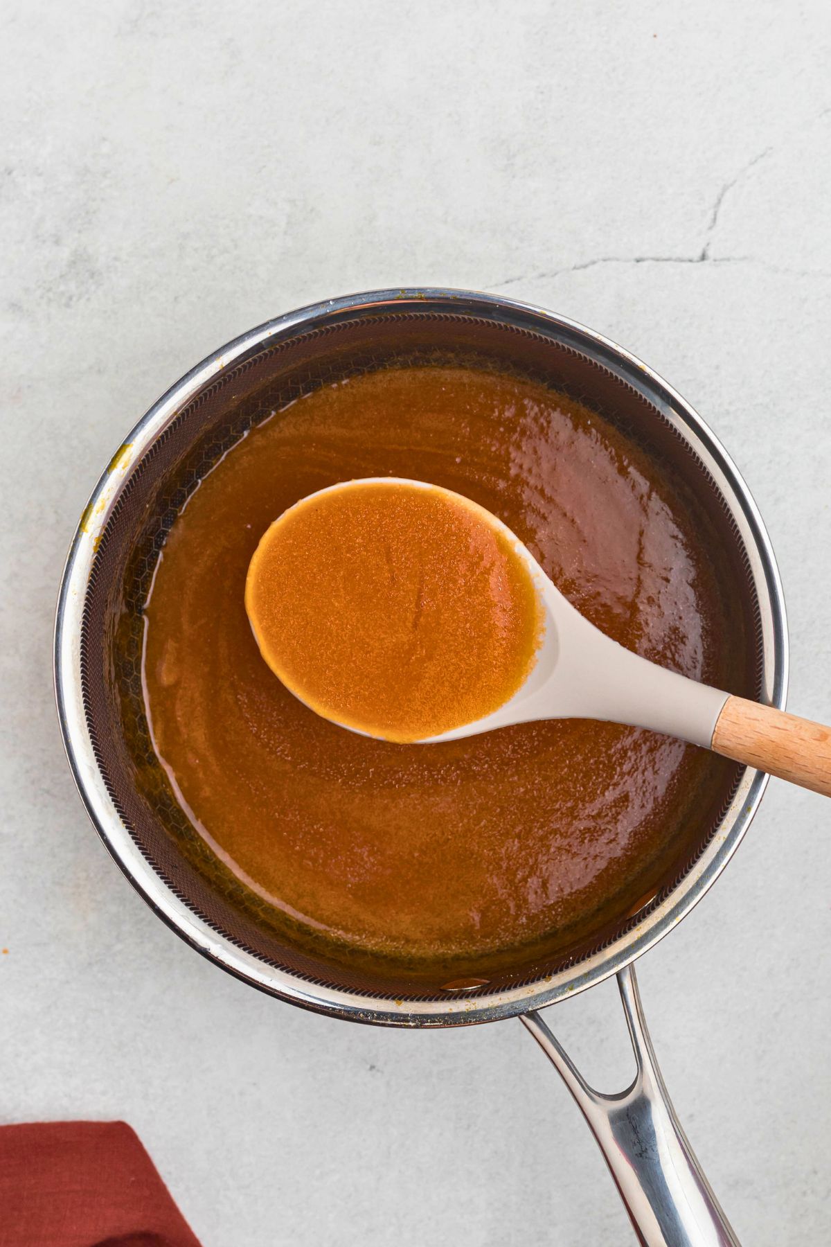 Creamy and buttery sauce in a saucepan, thickening after it's cooled, being spooned up with a serving spoon. 