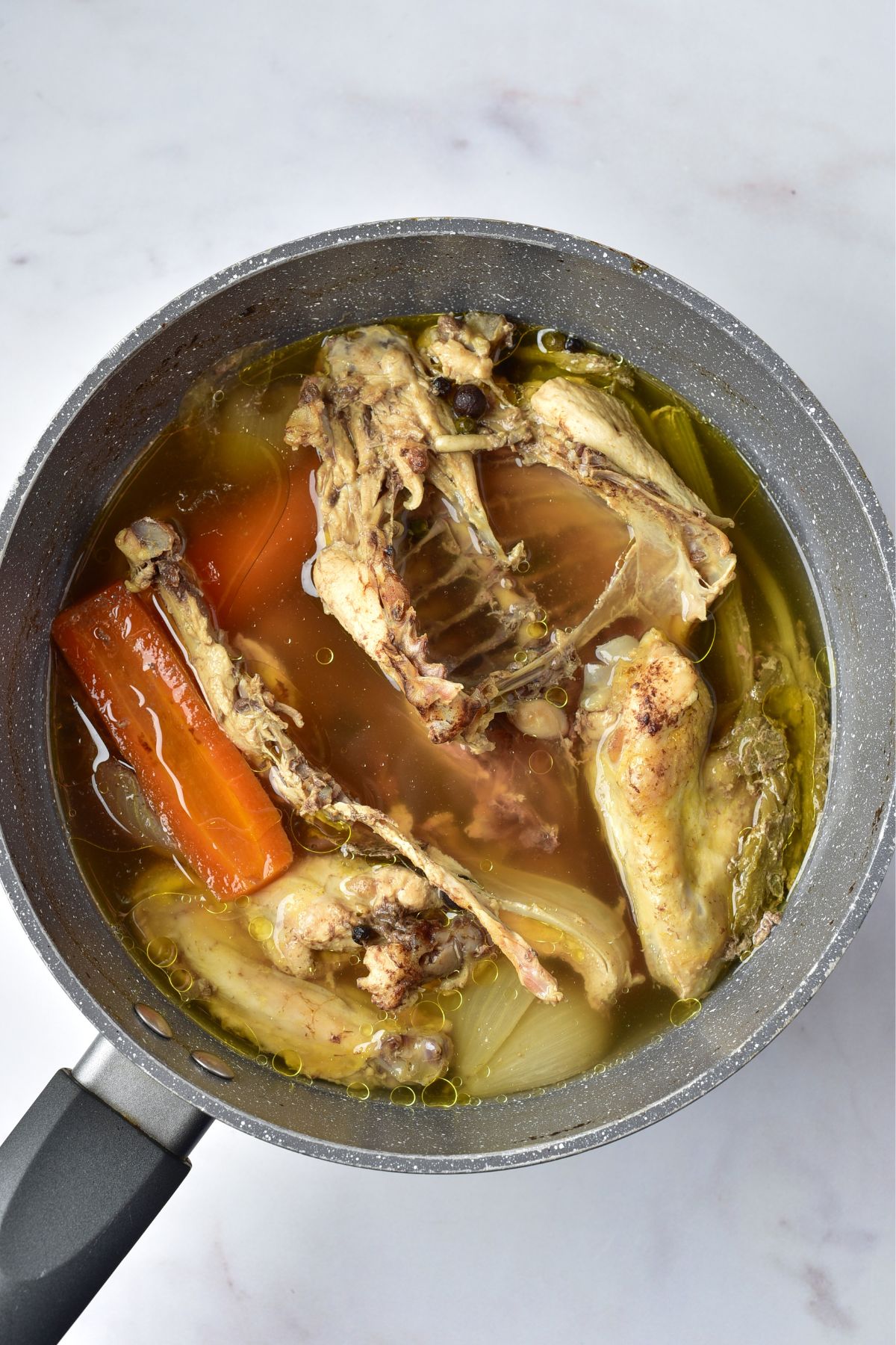 Stock pot with chicken, veggies, herbs, and water, that has been simmering  for over an hour. 