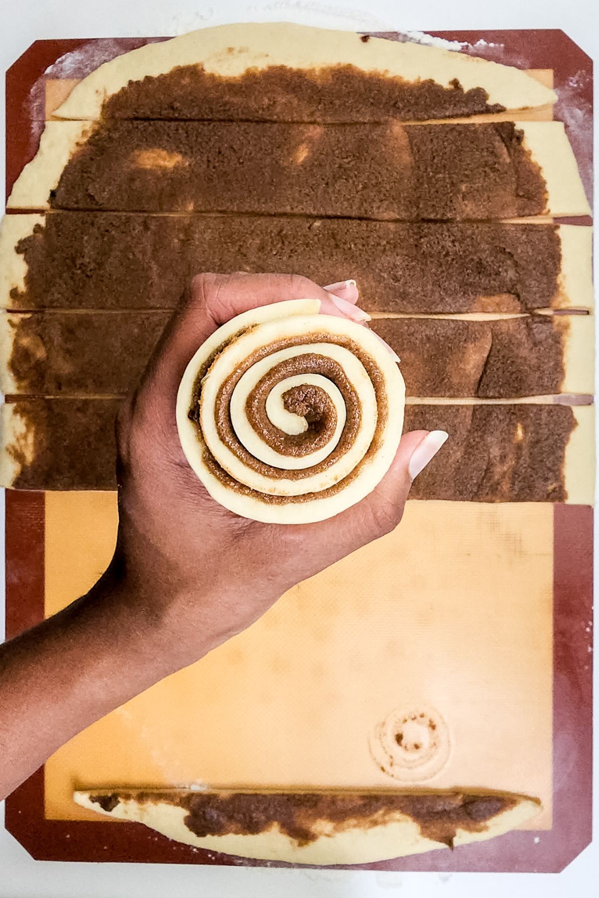 A hand hold a strip of dough that has been tightly wound into roll.