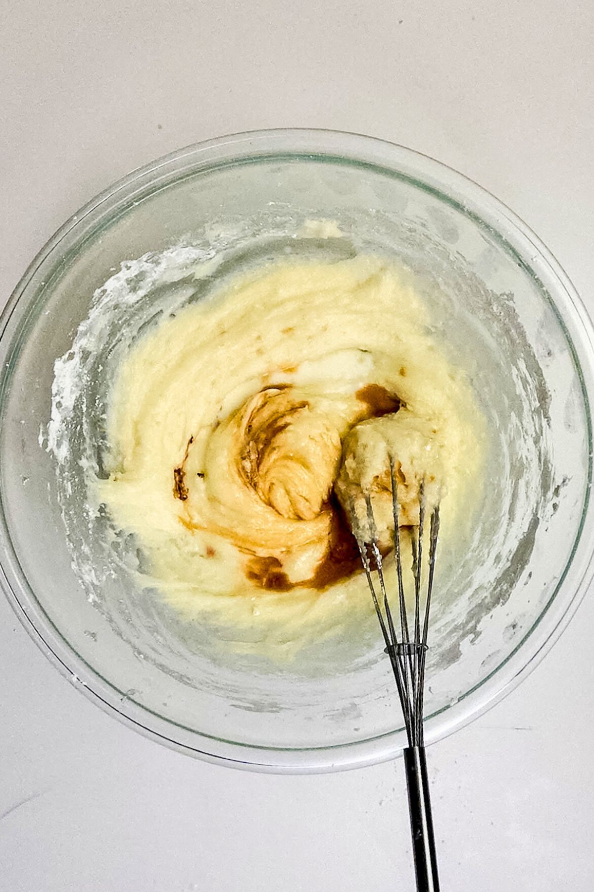 Cream cheese frosting being mixed together in a large clear glass bowl.