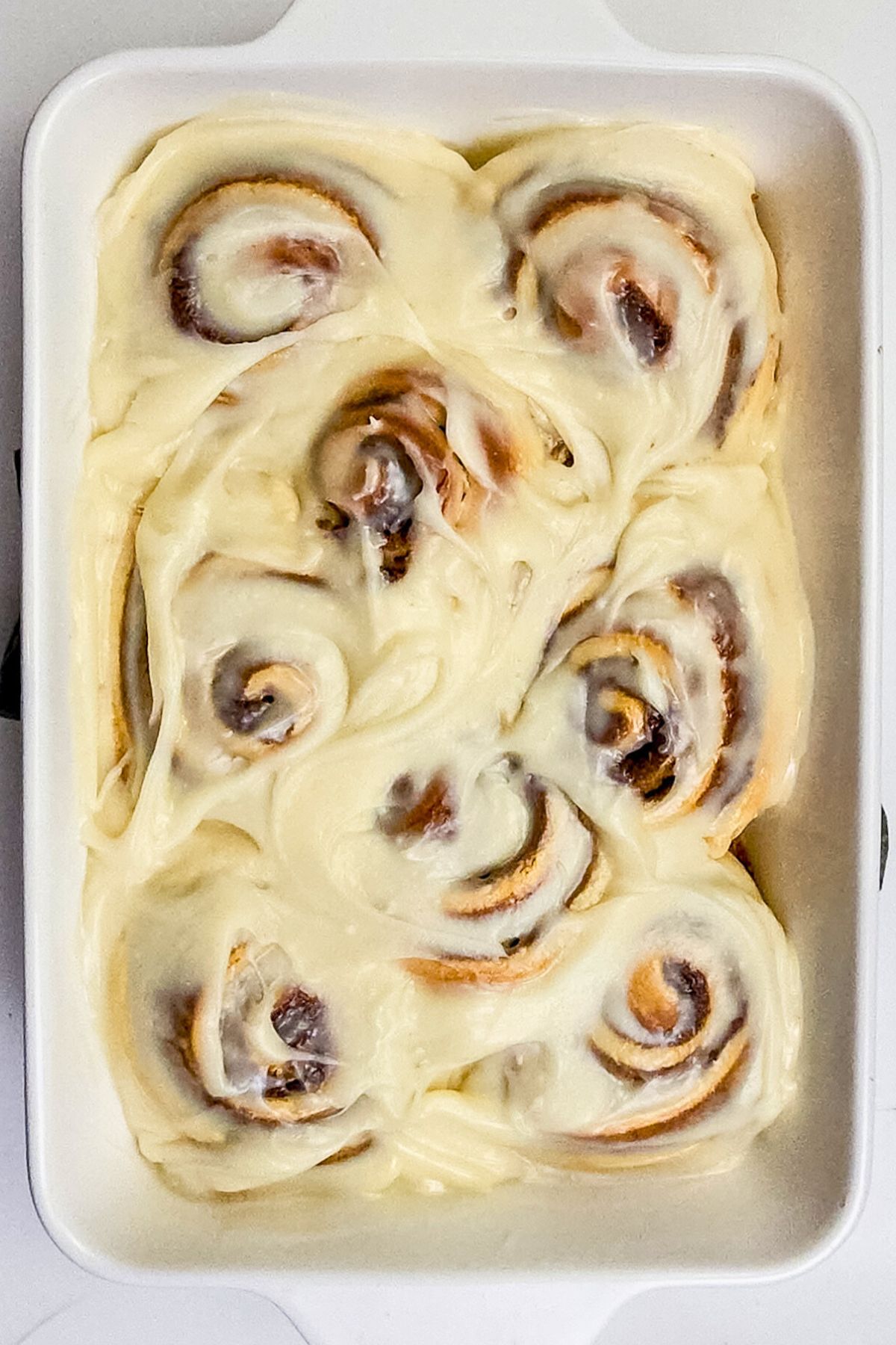 Cinnamon rolls in a white baking dish with cream cheese frosting on top.