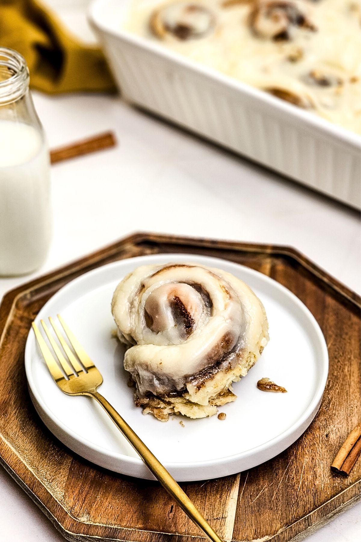 Cinnamon roll on a small white plate with a gold fork on the plate.