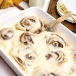 Gooey rolls in a white baking dish with frosting on top.