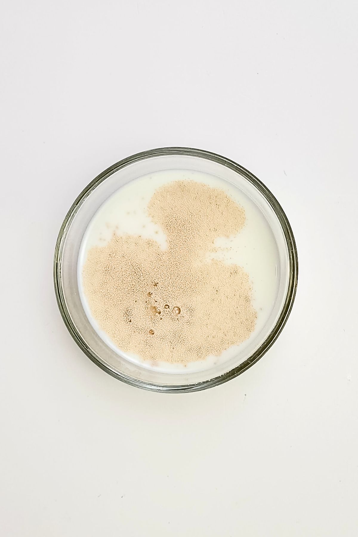 Yeast and warm milk in a clear glass bowl on a white marble table.