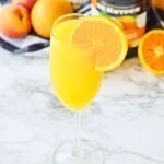 Peach mimosa with an orange slice for garnish on a white marble table.