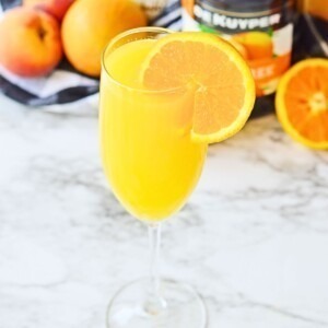 Peach mimosa with an orange slice for garnish on a white marble table.