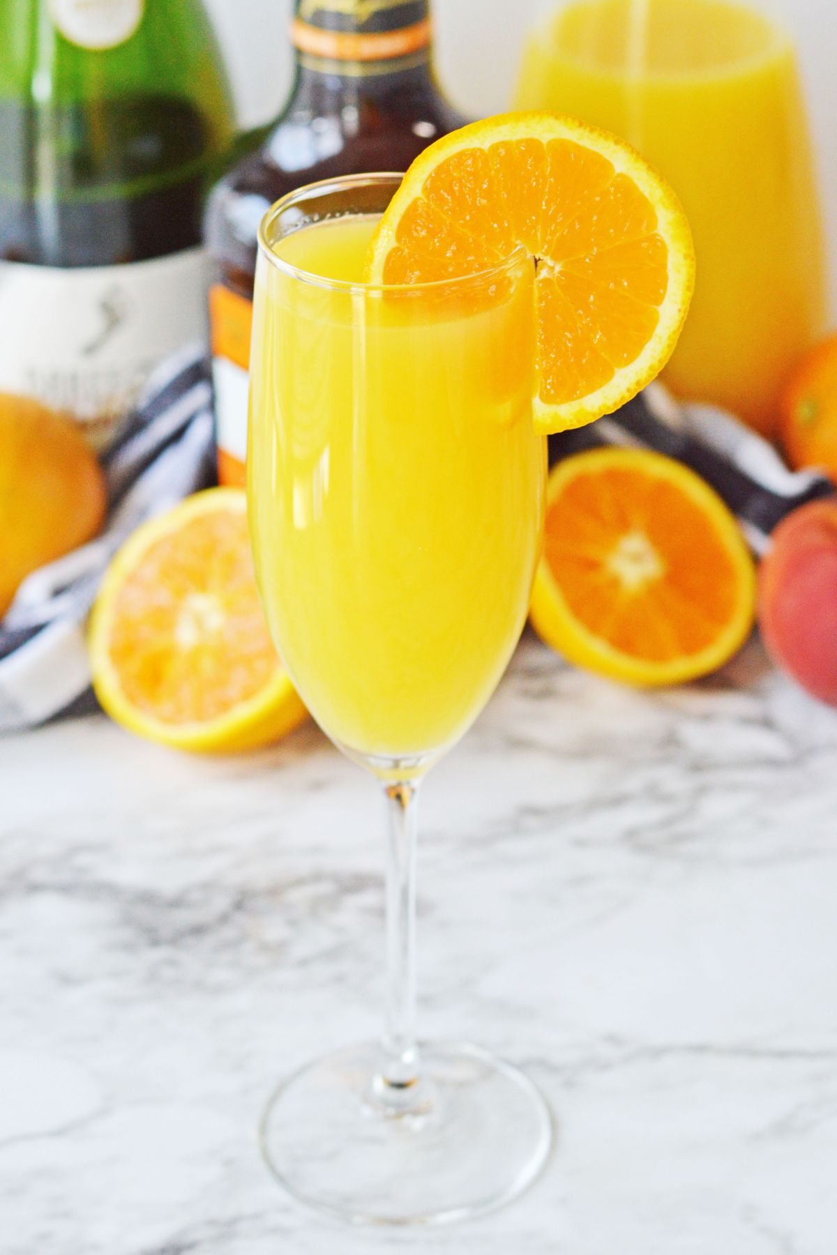 Peach mimosa with an orange slice for garnish on a white marble table.